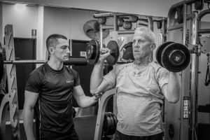 Personal Trainer Helping Client Weight Lift - Edge Fit