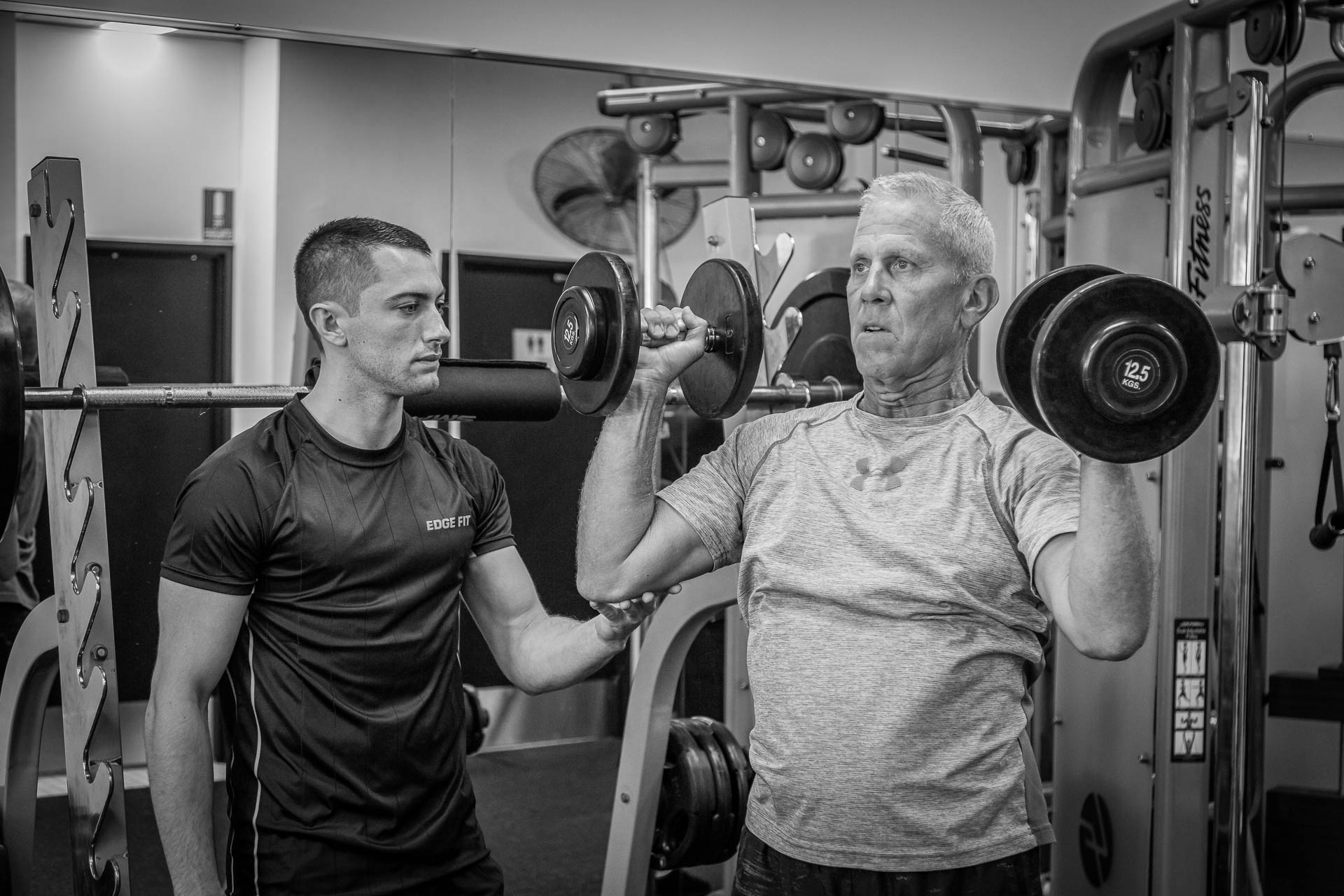 Personal Trainer Helping Client Weight Lift - Edge Fit