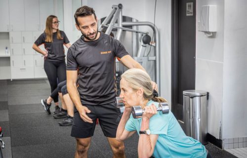Personal Trainer Help Client Through Exercise - Edge Fit